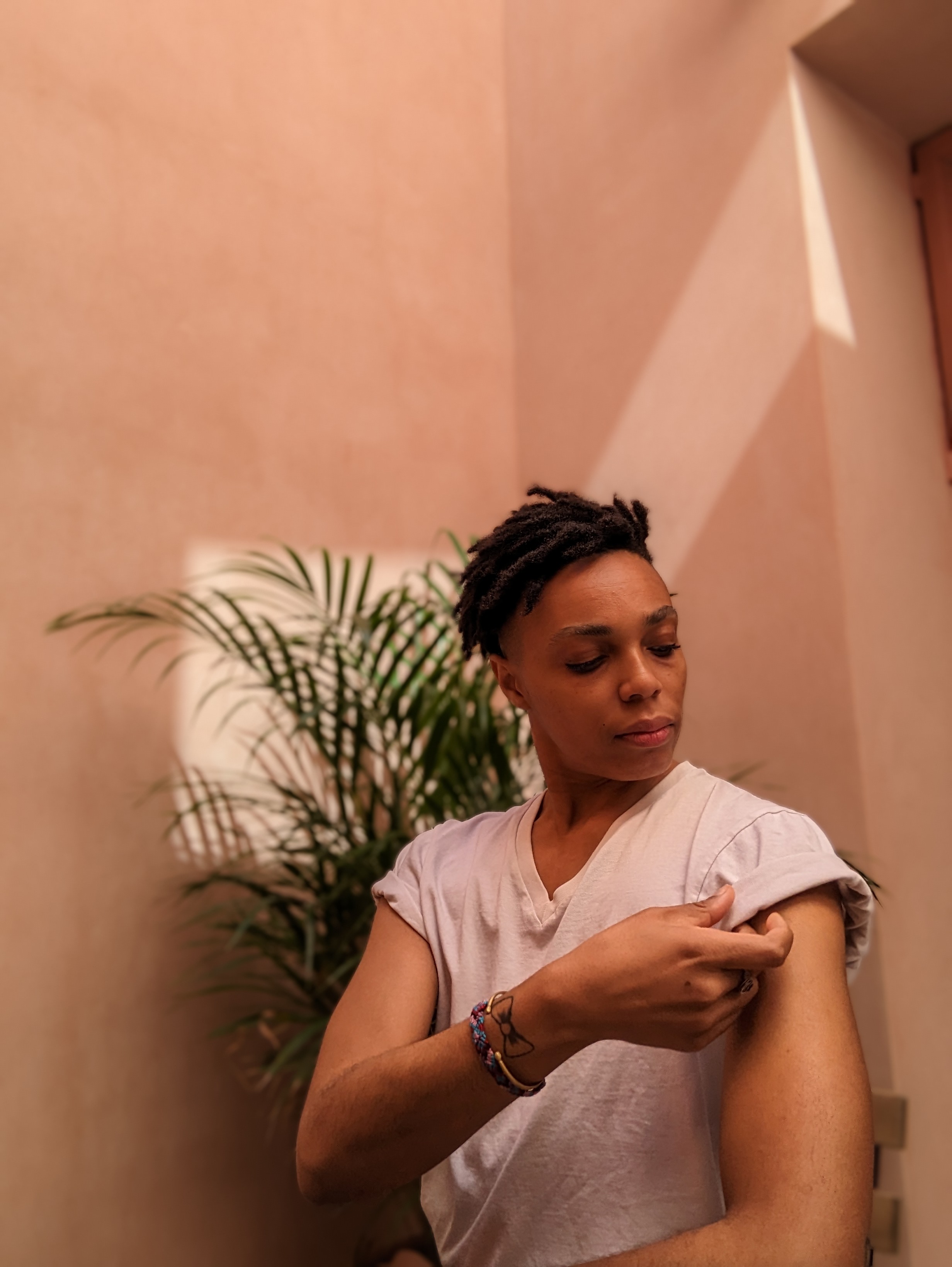 photo of zel in front of a pink wall adjusting the short sleeve of their white tshirt